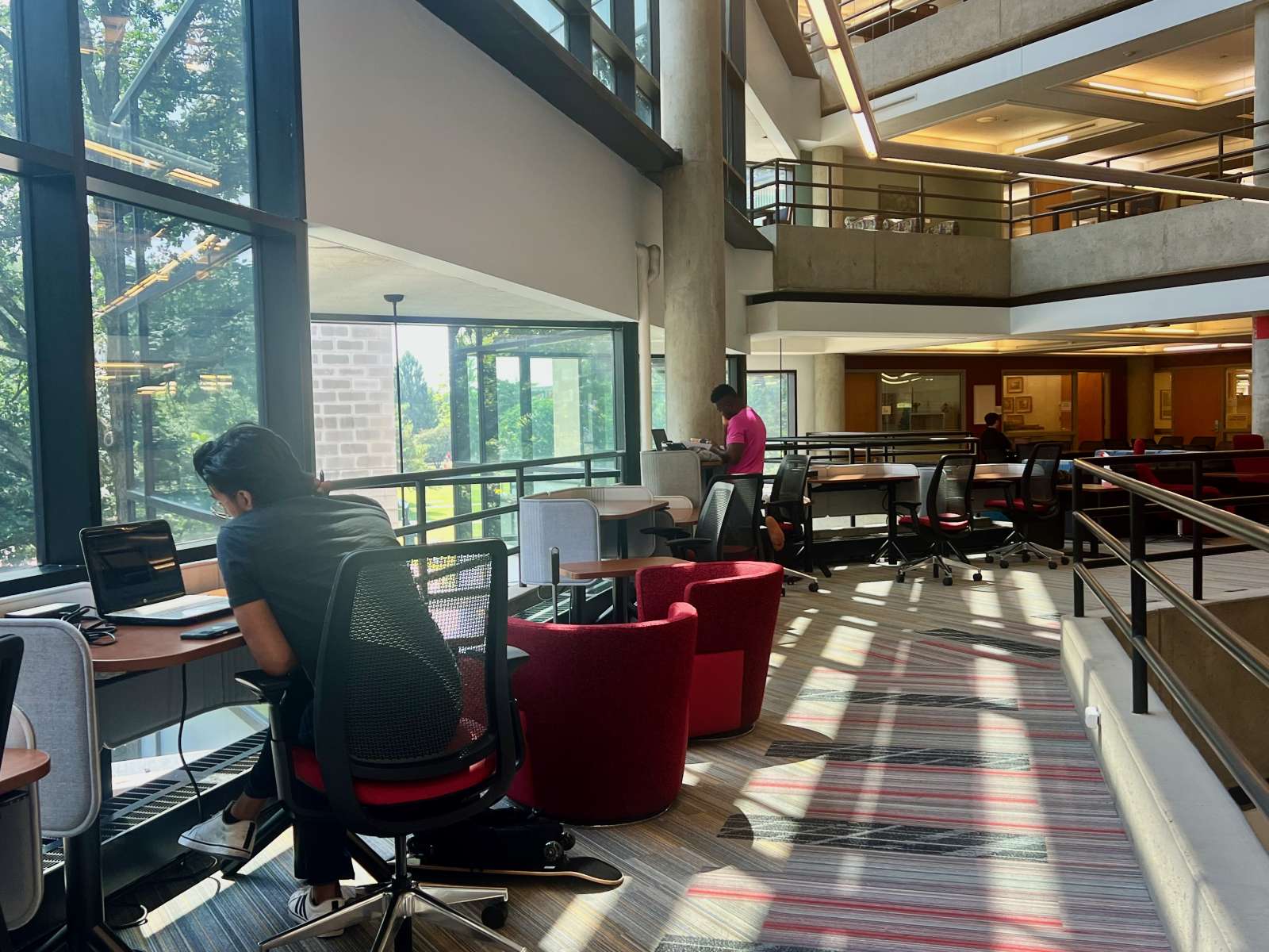 two students study at desks overlooking a sunlit window, one is standing and one is seated